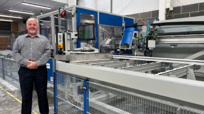 A man wearing a checkered shirt standing next to a large piece of machinery.